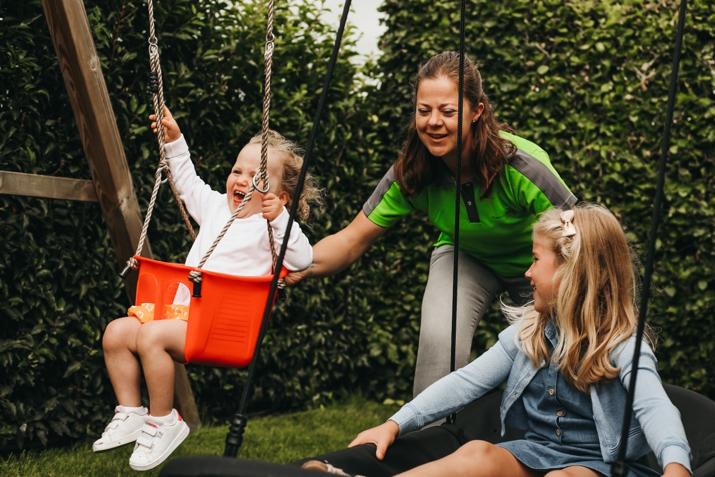 Een verzorgende van Familiezorg duwt twee jonge meisjes op hun schommel.