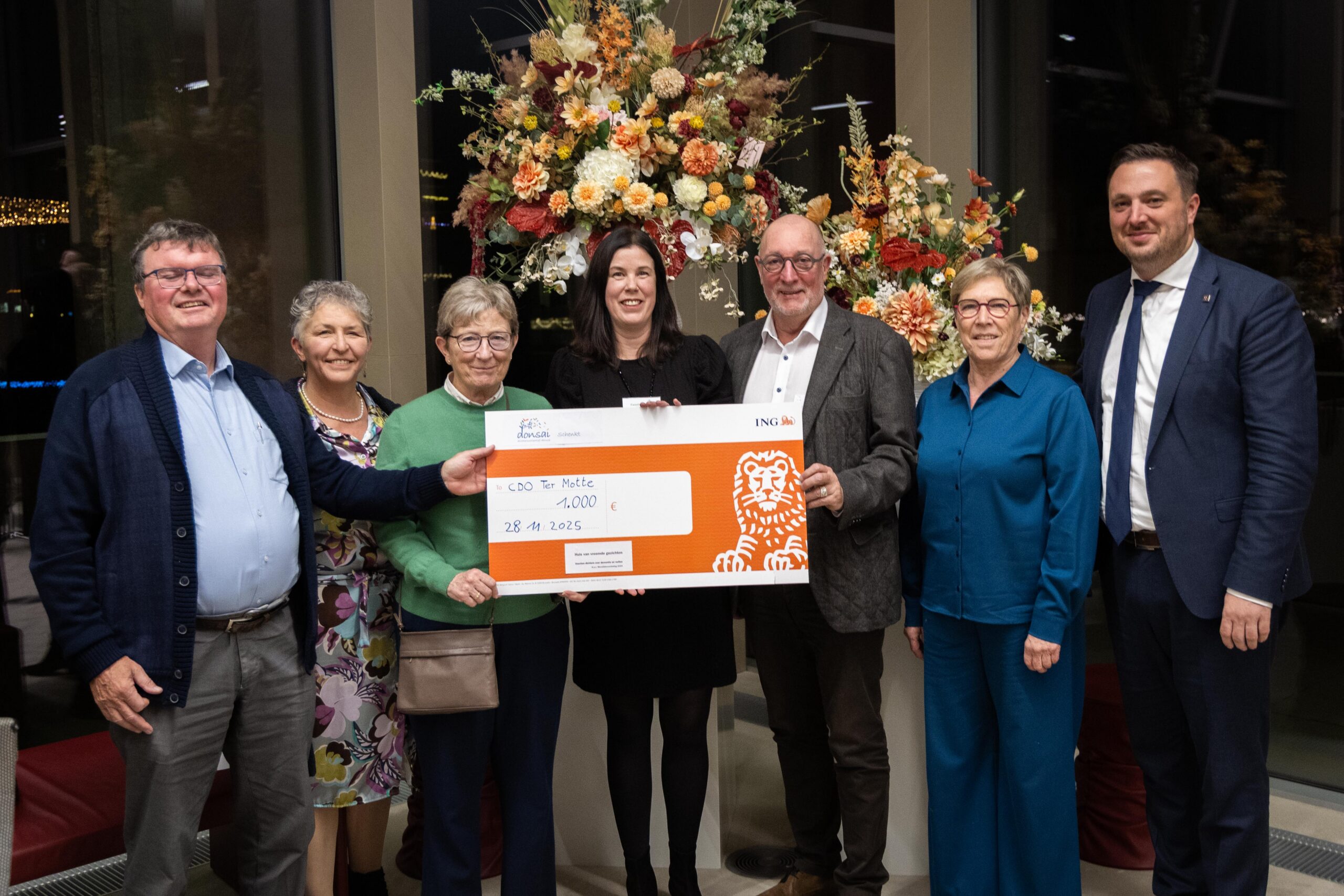 Foto van op het persmoment voor de fotovernissage 'Houvast'. Dichterscollectief Donsai schenkt een gift van 1.000 euro aan het project. Op de foto staan Evy Van Handenhoven (coördinator CDO Ter Motte), Mieke Ruys (algemeen directeur), Anne-Marie Dua (voorzitter Familiezorg), vertegenwoordiging van Donsai en burgemeester en schepen van Stad Deinze.