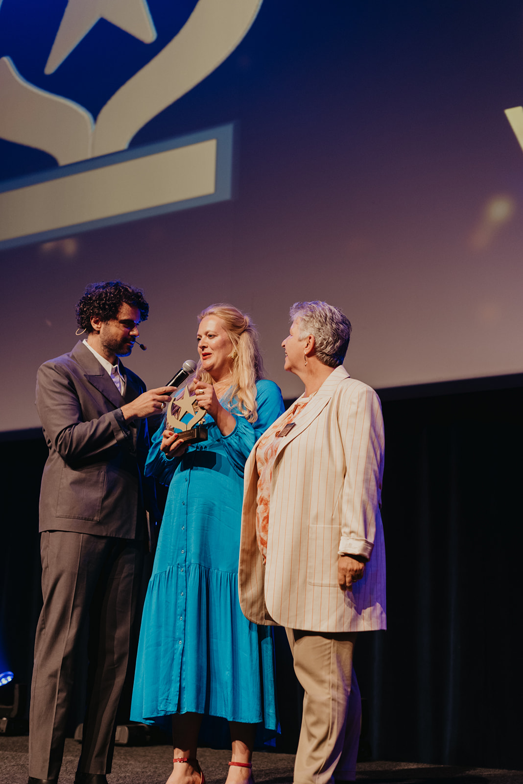 Kaat Flamée - communicatiemanager van Familiezorg - en Mieke Ruys - algemeen directeur - spreken Riadh Bahri toe na de winst voor Beste Marketing.