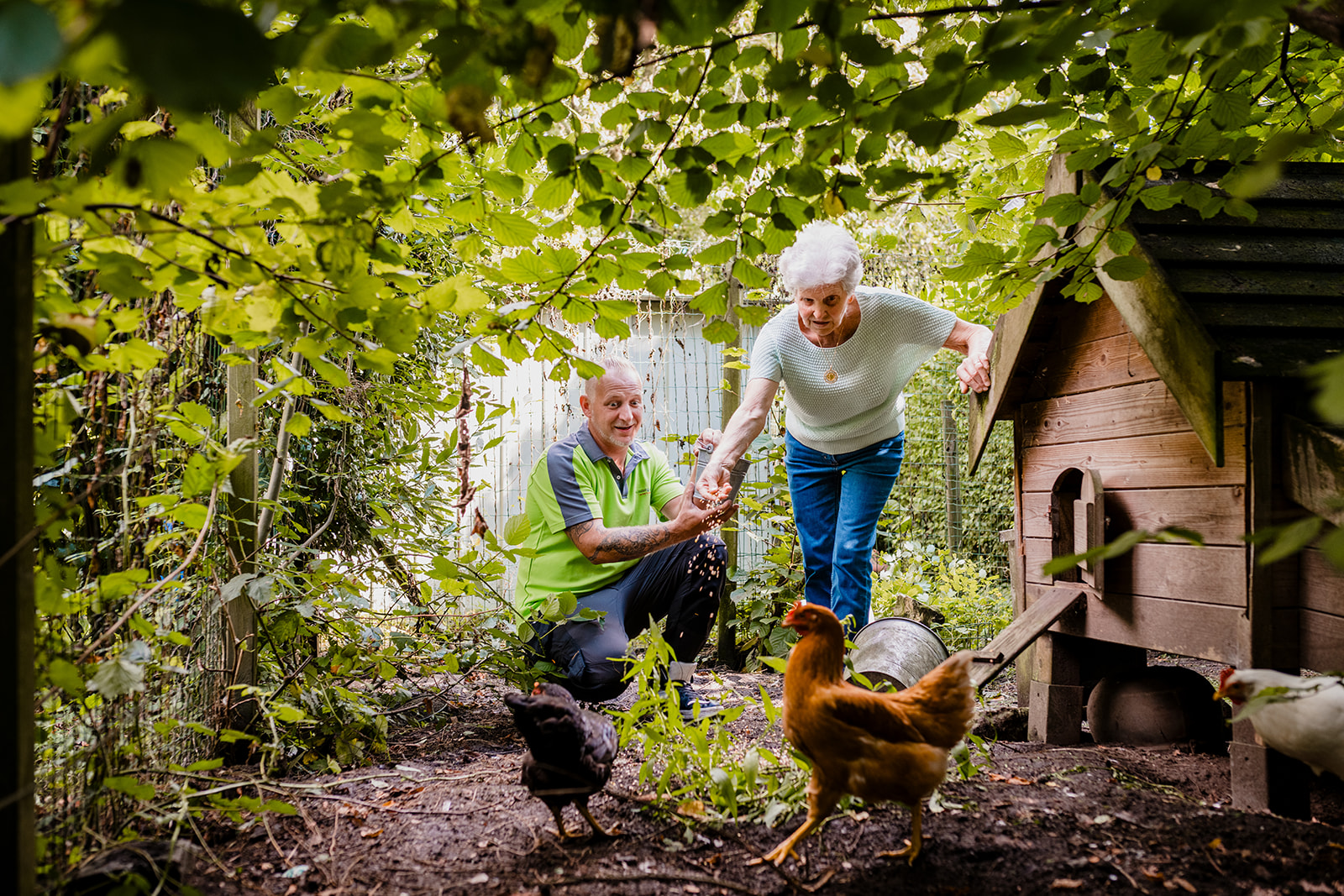 Een klusjesman van Familiezorg helpt een cliënte in haar kippenhok. Kippen eten geven.