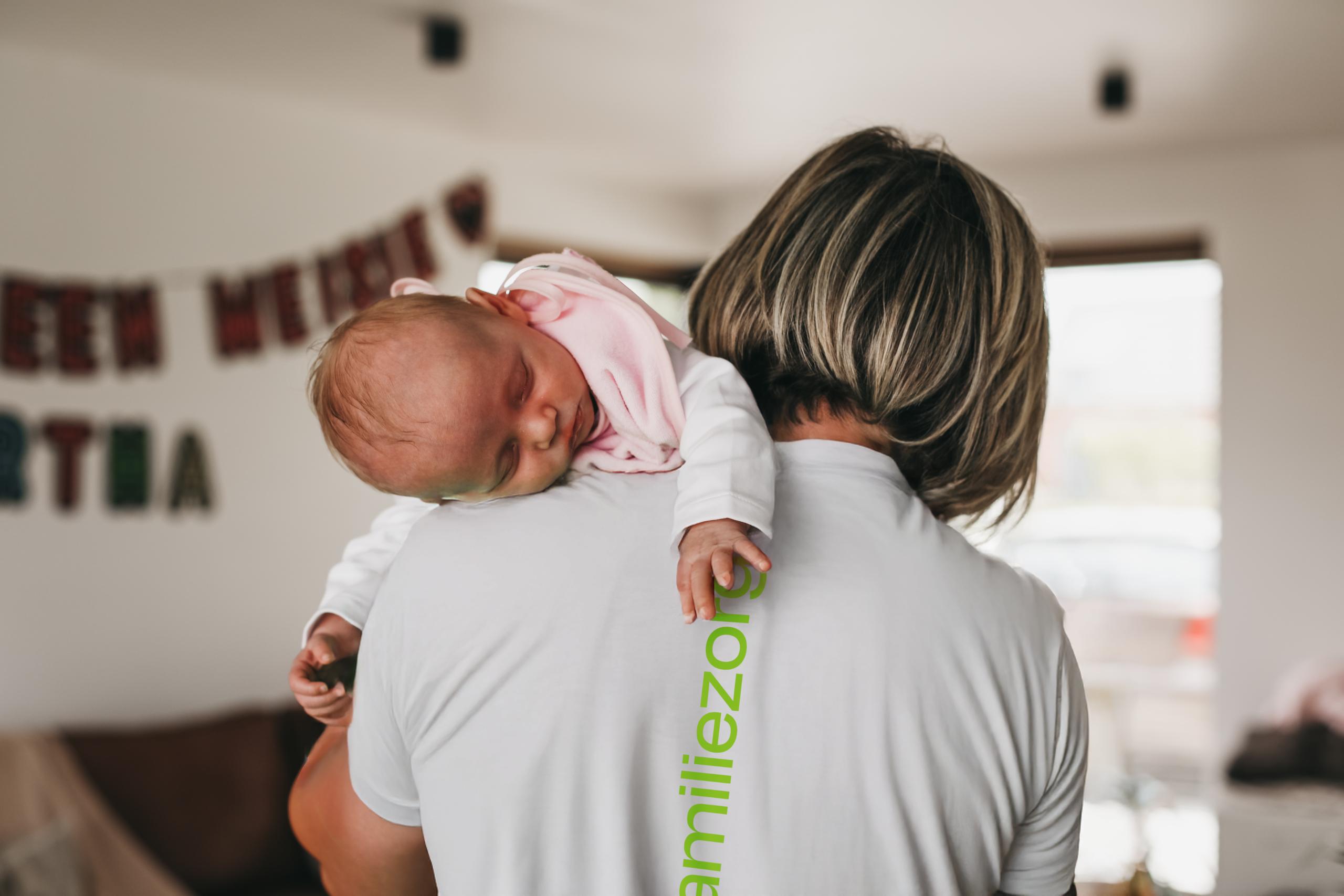 Baby slaapt over de schouder van een kraamverzorgende.