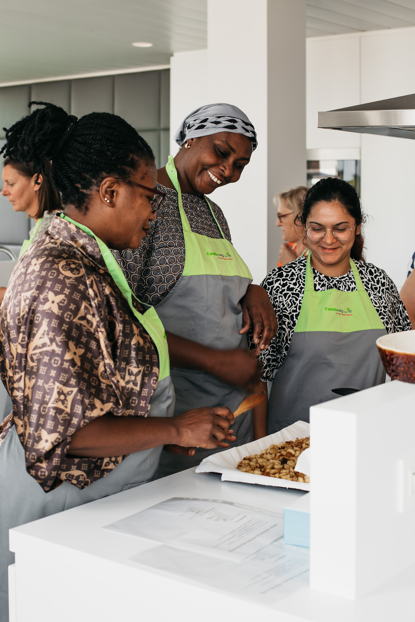 Drie cursisten van de opleiding tot verzorgende bij Familiezorg bekijken tevreden naar een bakplaat met granola.